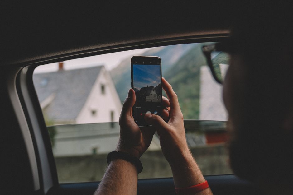 Person takes photo of scenic view from car window with smartphone in Norway.