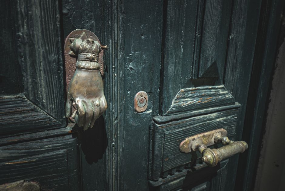 Intricate bronze hand-shaped door knocker on an aged wooden door with rustic details.