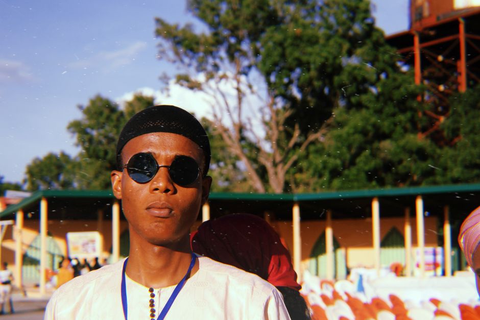 A confident young man poses in sunglasses at an outdoor event, embracing a sunny day.