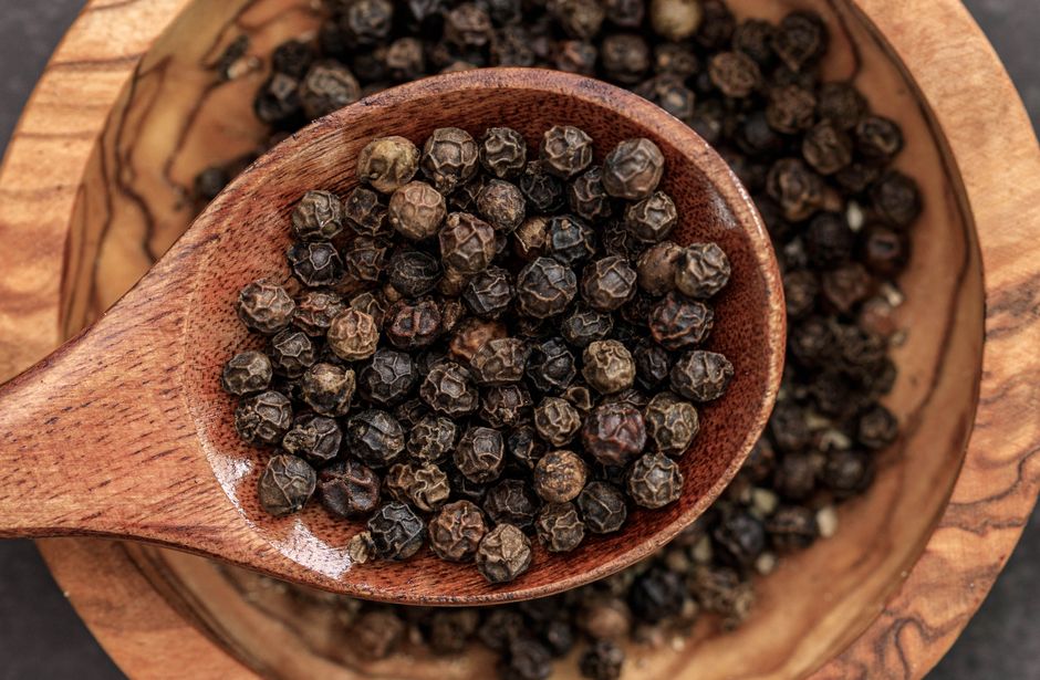 High-quality macro shot of black peppercorns in a wooden spoon on a bowl.