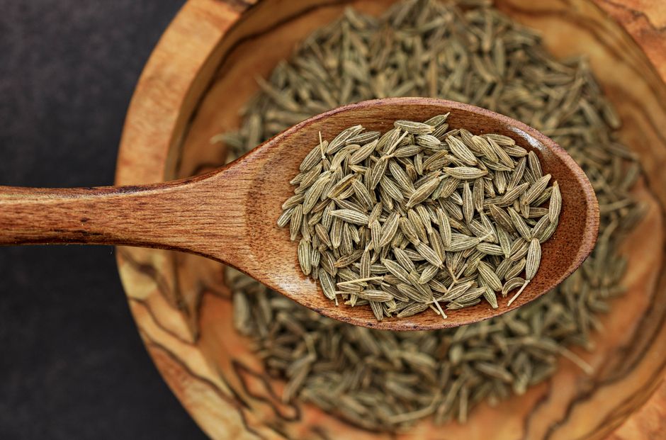 Detailed image of cumin seeds on a wooden spoon for culinary use.