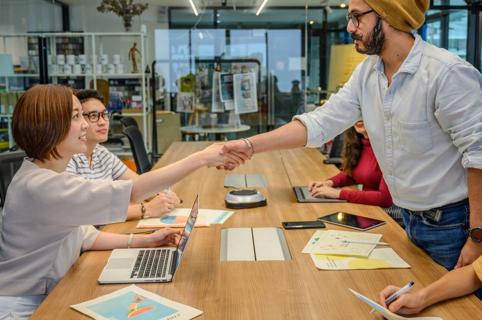 Diverse professionals in a modern office engaged in a collaborative meeting, shaking hands across a conference table.