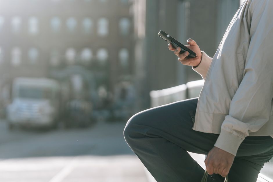 Side view of crop unrecognizable male with raised leg surfing internet on cellphone on roadway in sunny city