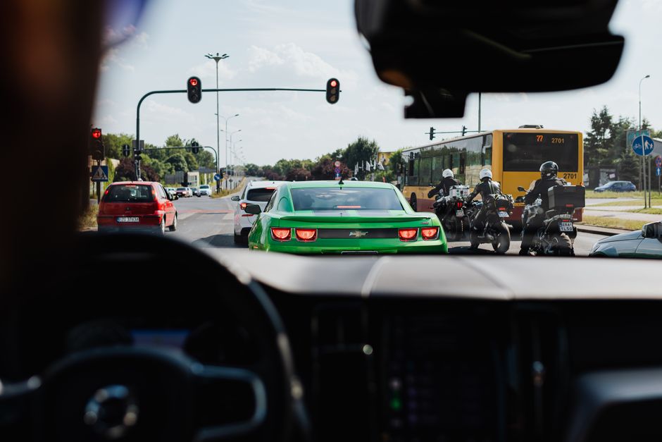 Street view of traffic with vehicles, bus, and motorcycles from a car's interior on a sunny day.