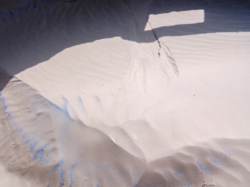 Close-up of sunlit beach sand featuring artistic patterns and shadows.