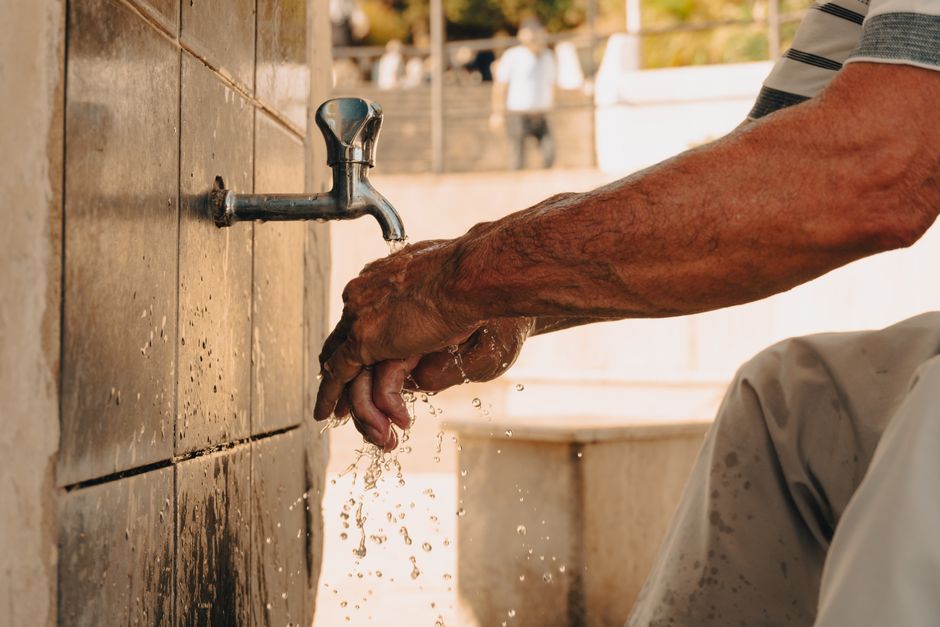 A person performing wudu, or Islamic ablution, washing hands at an outdoor tap.