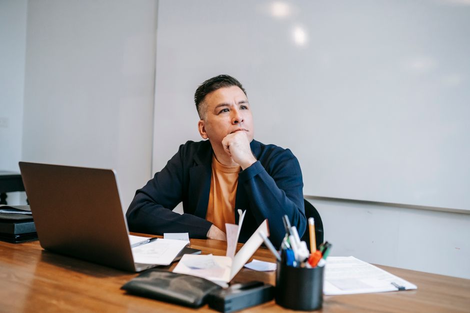 A thoughtful man in a home office setting, concentrating on his work with a laptop.