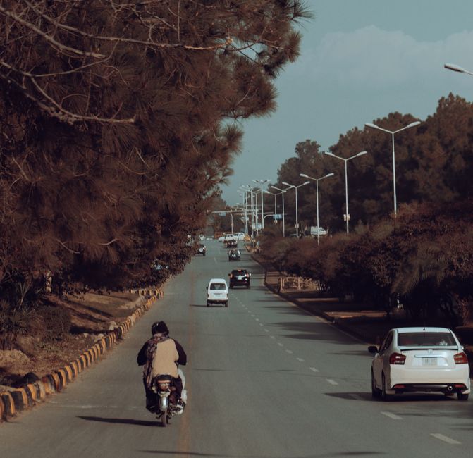 A scenic view of a tree-lined road in Islamabad, featuring light traffic during the fall season.