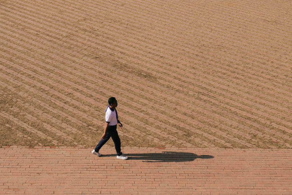 An individual walks across a patterned brick path, casting a long shadow.