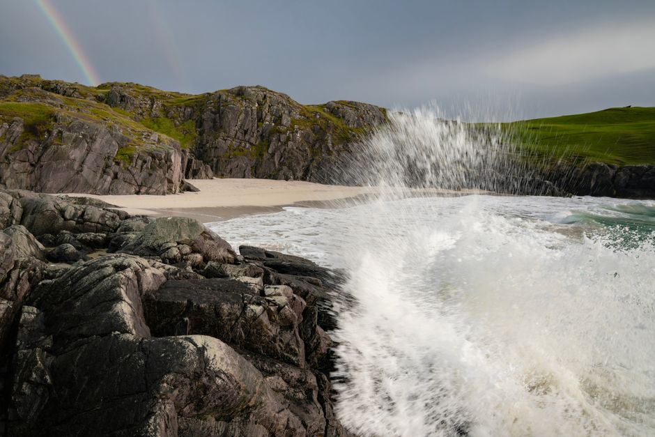 Captivating view of Scotland's coastline with crashing waves and a rainbow.