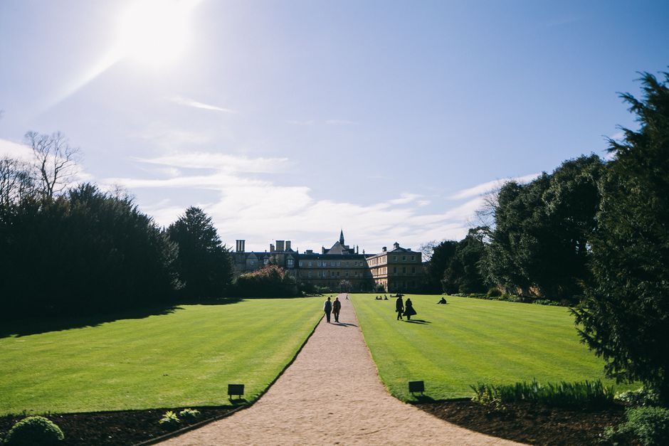 An idyllic walkway through lush gardens at Oxford University under bright sunlight.