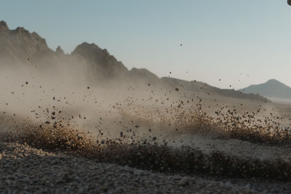 Close-up of dust cloud forming in rocky desert landscape with mountain backdrop.