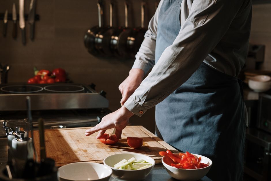 Chef slicing fresh tomatoes and peppers on a wooden board in the kitchen.