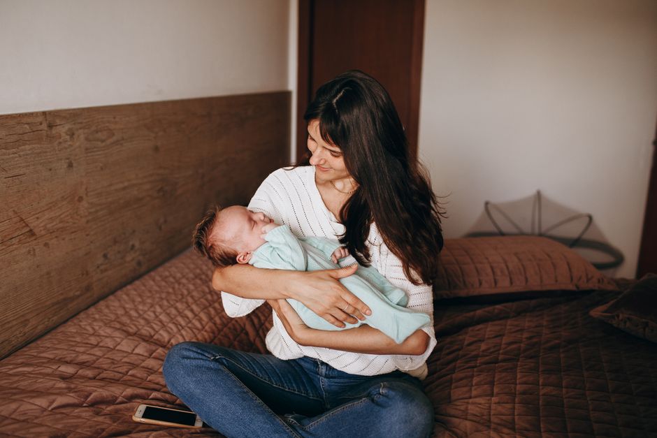 A mother lovingly cradles her sleeping baby while sitting on a bed, embodying warmth and intimacy.