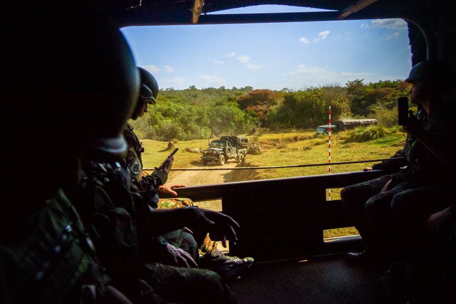 Military personnel inside an armored vehicle observing outdoor exercises on a sunny day.