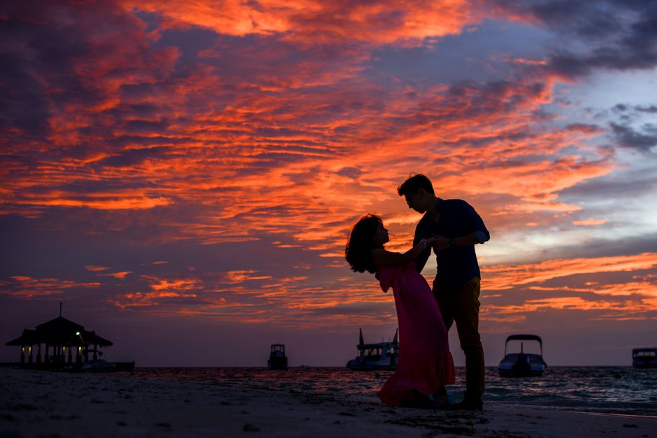 Silhouetted couple sharing a romantic moment on the beach during a stunning sunset.