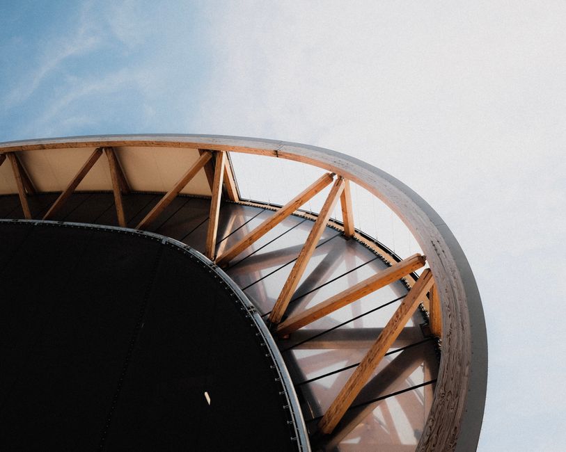 Low angle view of modern architectural facade with curved design and wooden beams against a clear blue sky.
