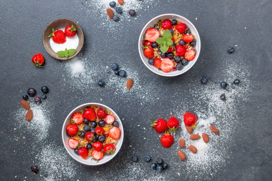 Top view of fresh berry and almond bowls with sugar on dark slate.