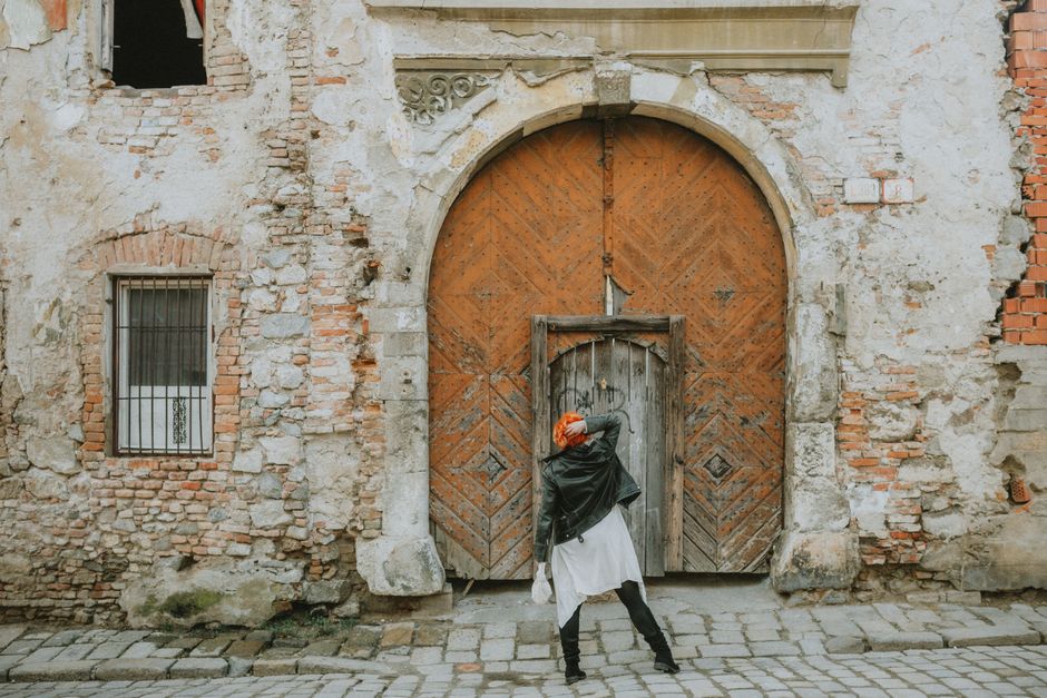 Woman standing at old wooden gate in historic Bratislava street, showcasing urban decay.