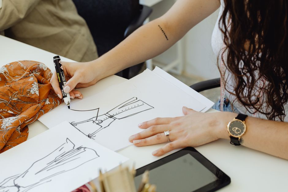 Fashion designer sketching dress ideas at a desk with fabric and sketches.