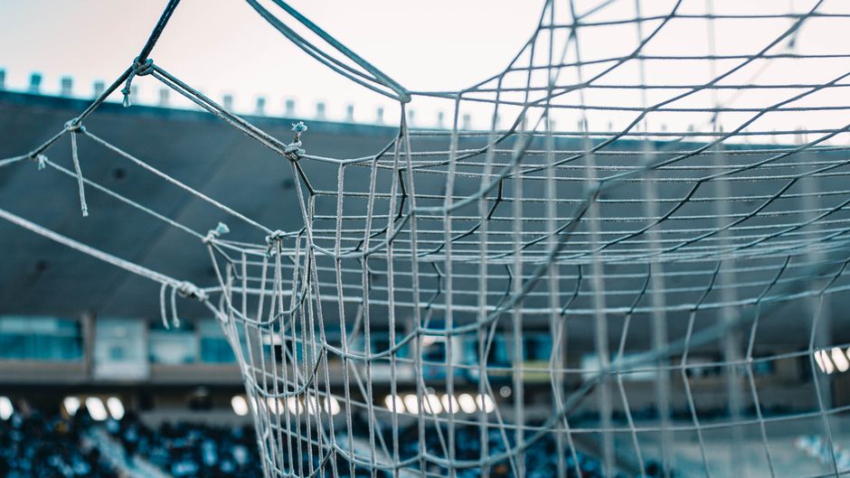 A detailed view of a soccer net with stadium seating in the background.
