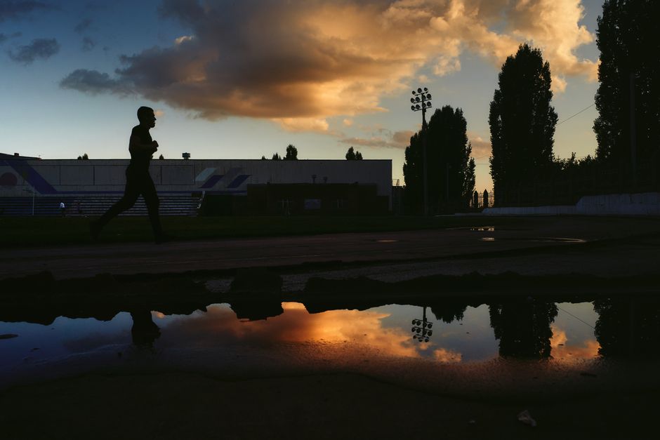 A silhouette of a man running on a track with a dramatic sunset sky reflected in puddles.