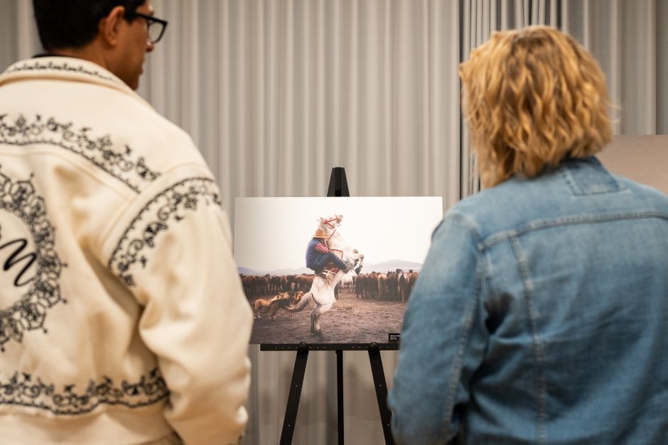 Two adults admire a photo of a rider on a horse at an indoor exhibition.