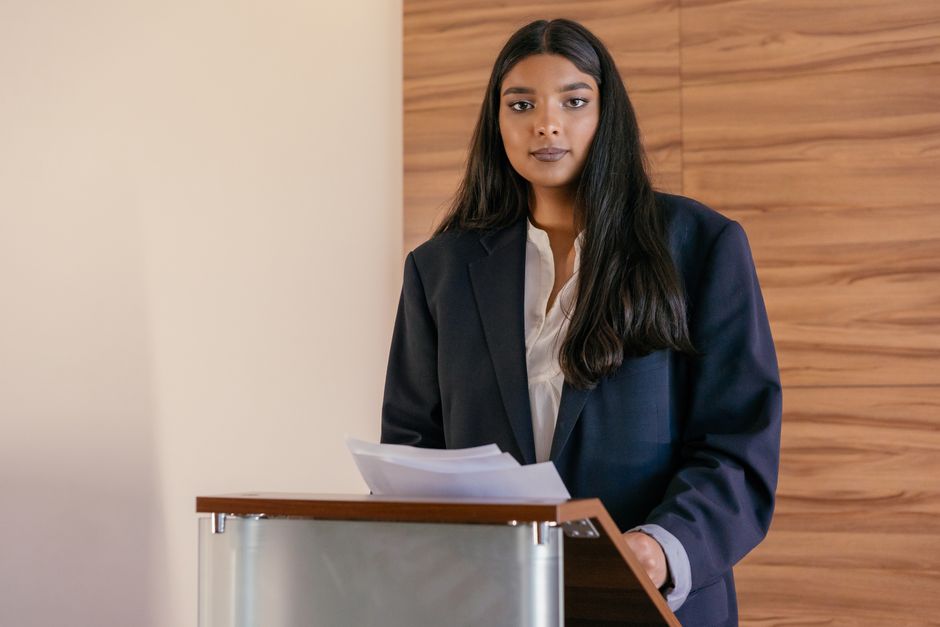 Woman in a suit presenting at a podium, symbolizing leadership and empowerment.
