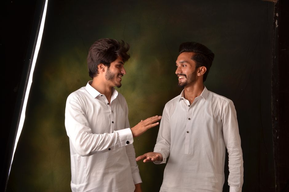 Two men in white shirts smiling and talking in a studio portrait.