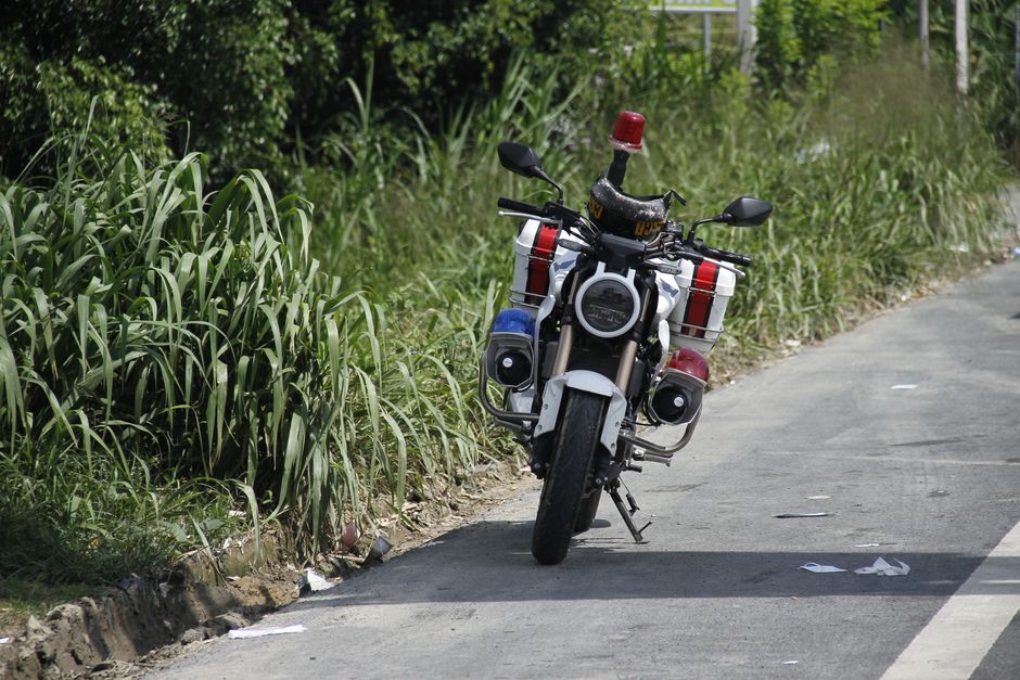 A police motorcycle stands parked by a rural roadside, surrounded by lush greenery.