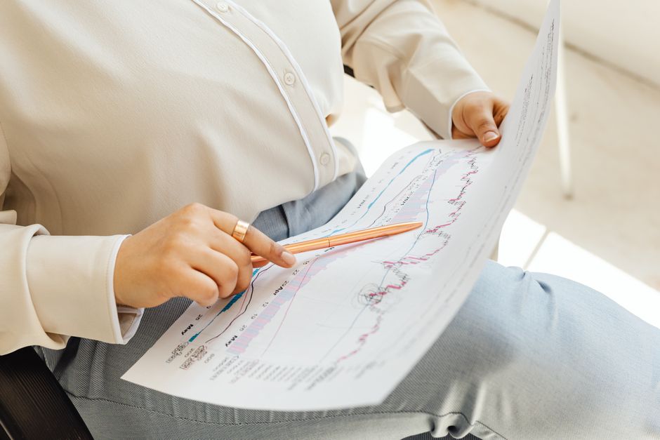 Close-up of hands holding and analyzing finance charts with pen.