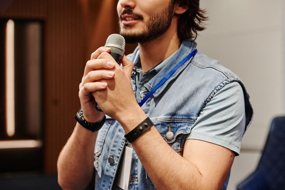 Man with a beard speaks into a microphone during an indoor seminar or presentation.