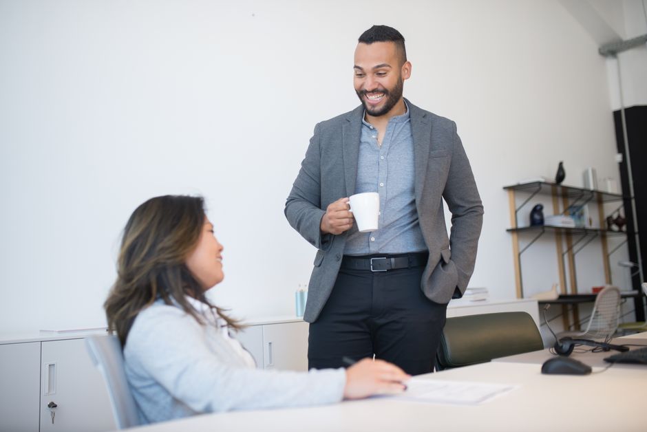Two business professionals smiling and talking during a coffee break in a modern office setting.