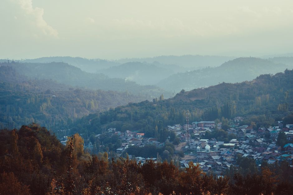 A serene view of Srinagar's mist-covered hills and lush landscape, showcasing a tranquil townscape.