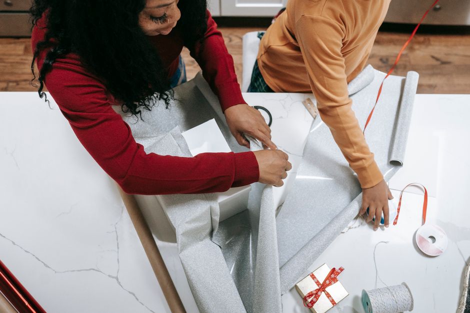 From above of crop anonymous African American mother and child engaged in Christmas preparation packing box of present