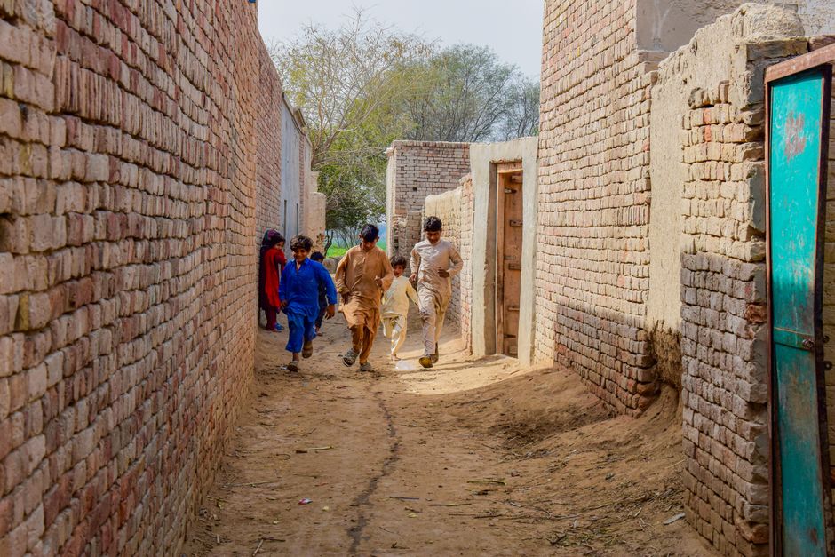 Group of boys walking through a narrow alley between brick walls in Jalalpur Pirwala, Punjab, Pakistan.