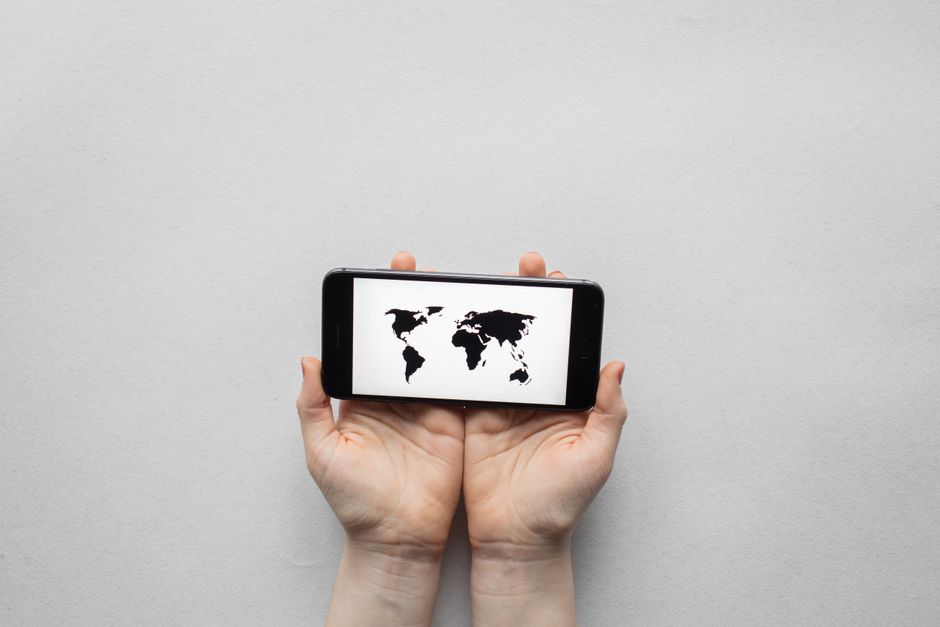 Hands holding a smartphone displaying a world map on a white background.