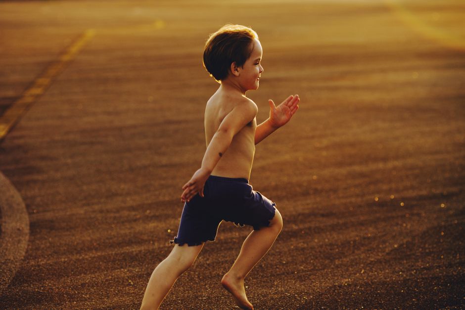 A young boy runs barefoot on a sunlit outdoor track, embodying energy and freedom.