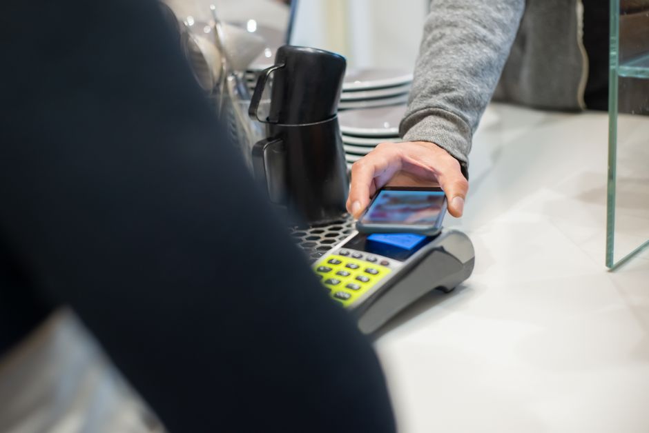 A customer makes a contactless payment using a smartphone at a café, showcasing modern digital transactions.