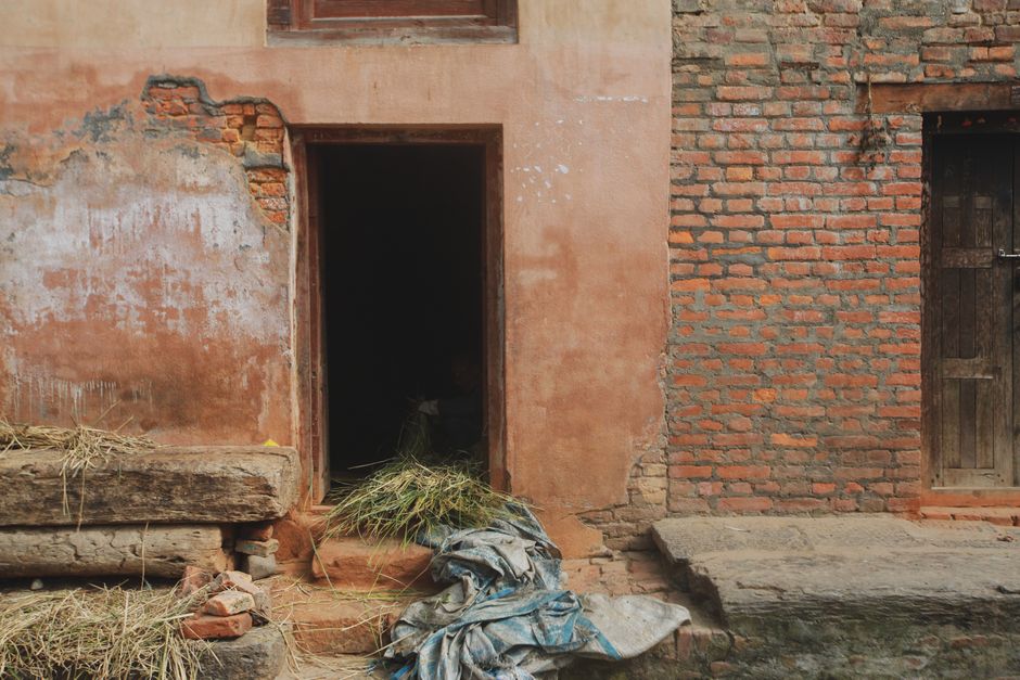 A rustic brick building with an open doorway, displaying hay and worn materials, evokes a rural and nostalgic feel.