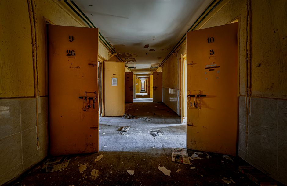 A dimly lit, abandoned prison corridor with open cell doors and debris on the floor.