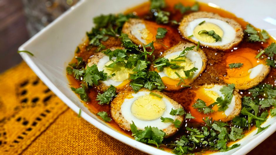 Delicious spicy egg curry garnished with fresh cilantro in a white bowl, featuring vibrant colors and rich flavors.