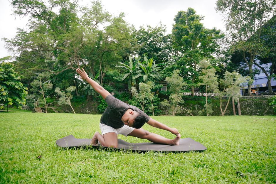 A man performs a yoga stretch in a serene outdoor garden setting, emphasizing fitness and nature connection.