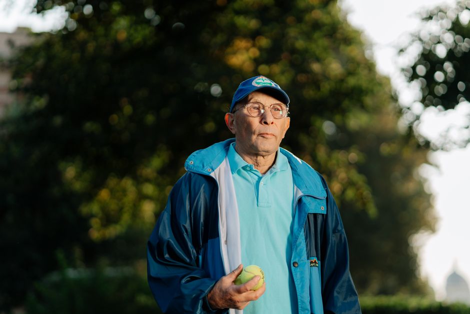 A senior man holding a tennis ball and enjoying leisure time outside in a park.