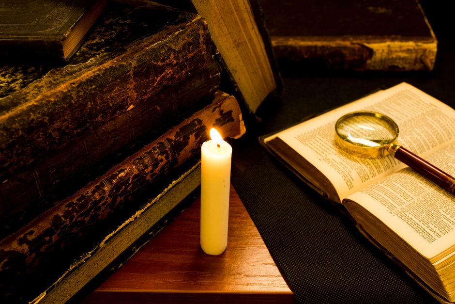 Cozy candlelit vignette with vintage books and magnifying glass, evoking a sense of history and mystery.
