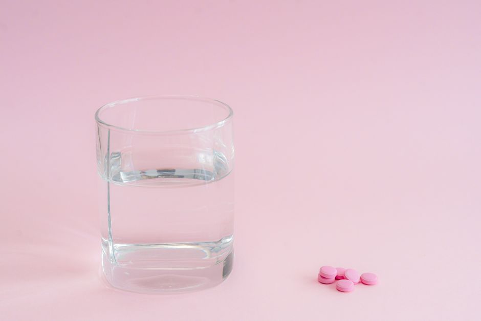 Minimalist image of a glass of water and pink pills on a pastel background, suitable for health themes.
