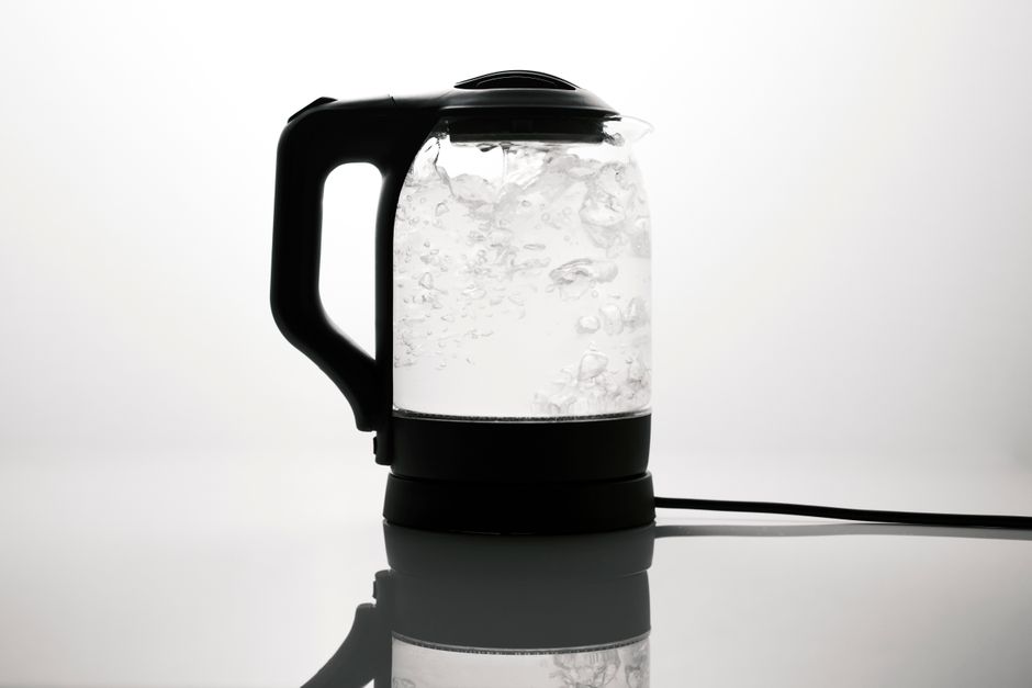 A sleek electric kettle boiling water, captured on a reflective white surface.