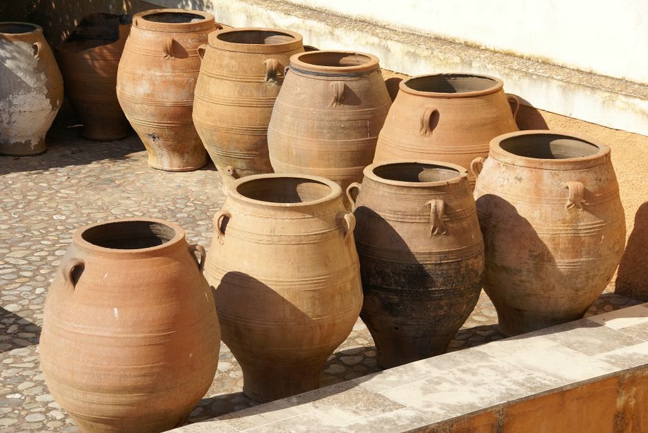 A collection of traditional Cretan clay jars displayed outdoors in a sunlit courtyard.