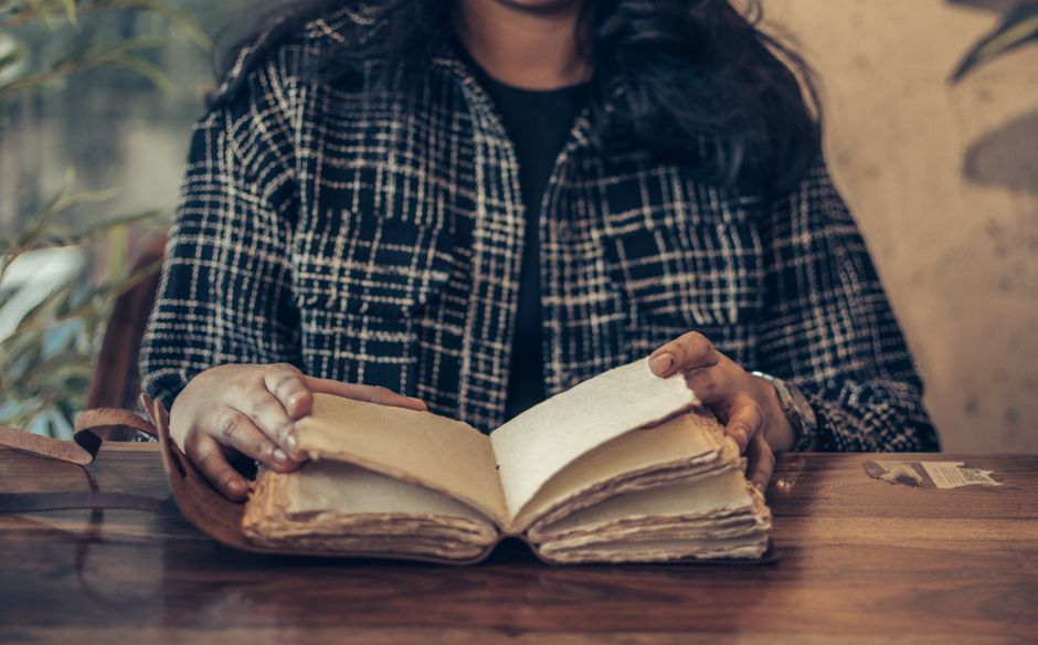 A person reading an old vintage book while seated at a wooden desk indoors, evoking a retro literature vibe.