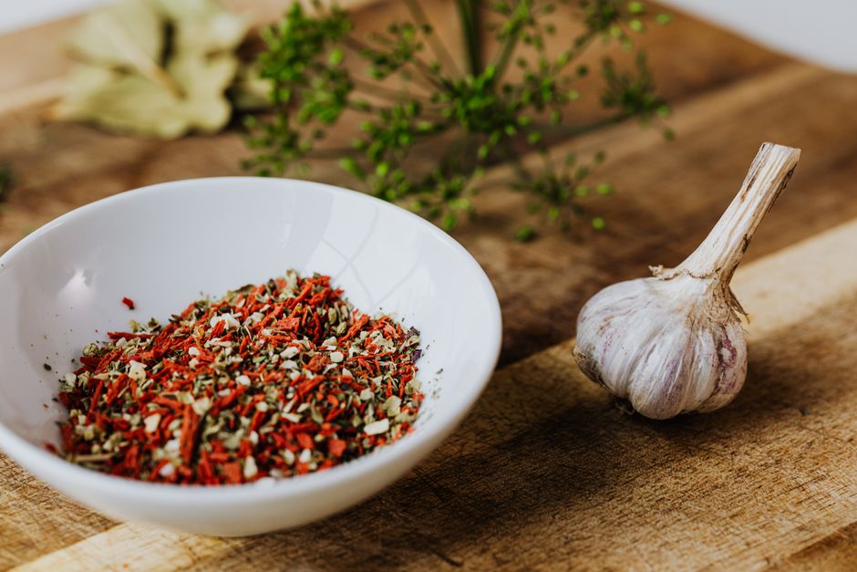 Aromatic spices in a white bowl alongside garlic on a rustic wooden tray.